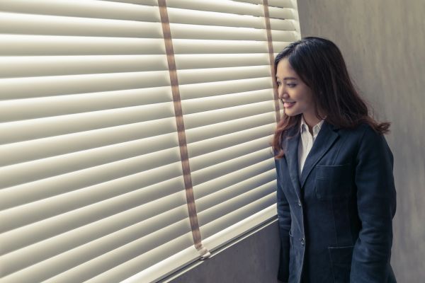 Professional woman looking at window blinds